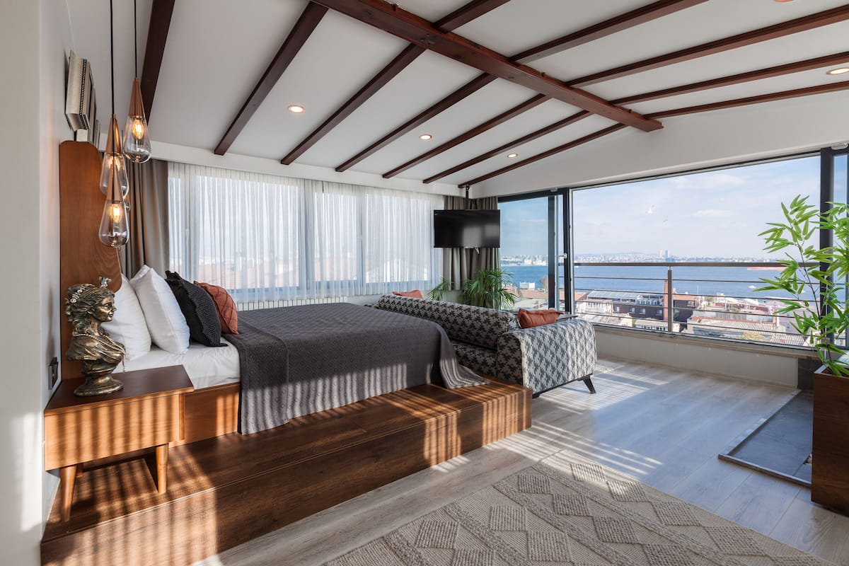A modern bedroom with a large bed, a sofa, a TV, and a view of the city.