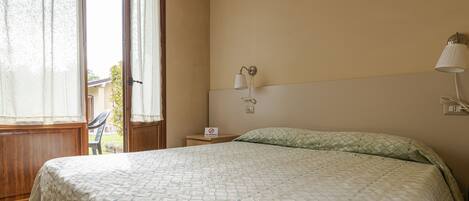 Un dormitorio con cama, mesita de noche, lámpara y ventana con cortinas.