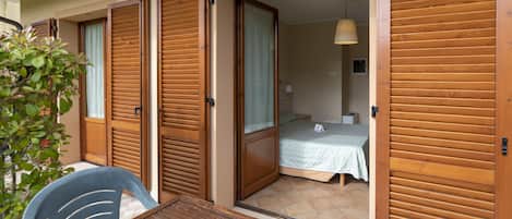 A room with a bed, a table, and a chair. There is a door leading to another room.