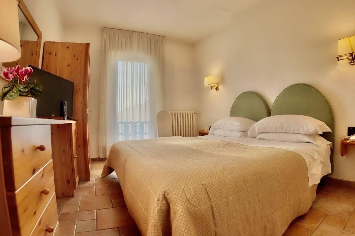 Une chambre d’hôtel comprenant un lit, une commode, un miroir, une fenêtre avec des rideaux et une lampe fixée au mur.