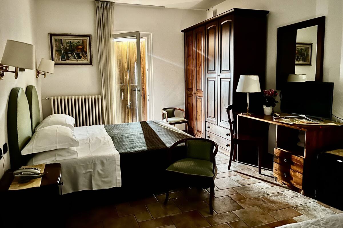 Une chambre d’hôtel comprenant un lit, un bureau avec une lampe, une chaise, une armoire et un radiateur.