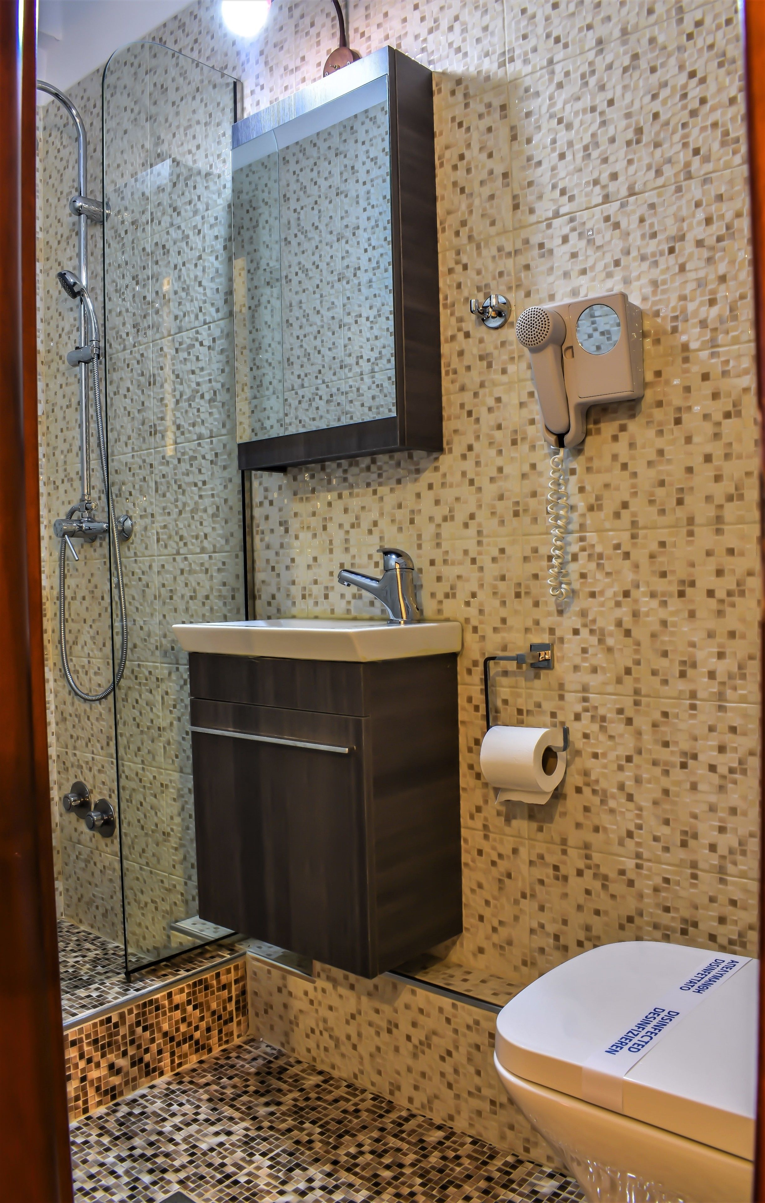 Un baño con ducha, lavamanos, inodoro y un secador de pelo en la pared.
