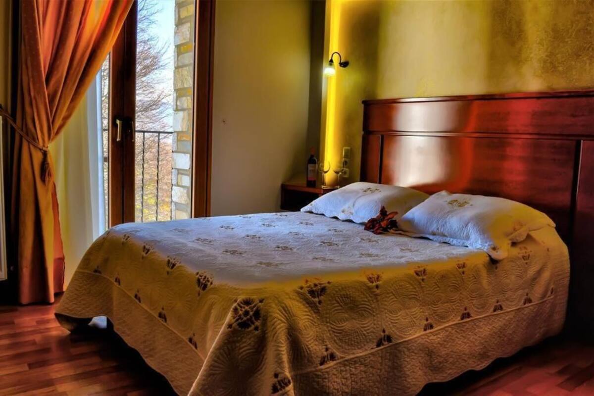 A bed with a patterned bedspread, a nightstand with a bottle and glasses, and a wall-mounted light fixture.