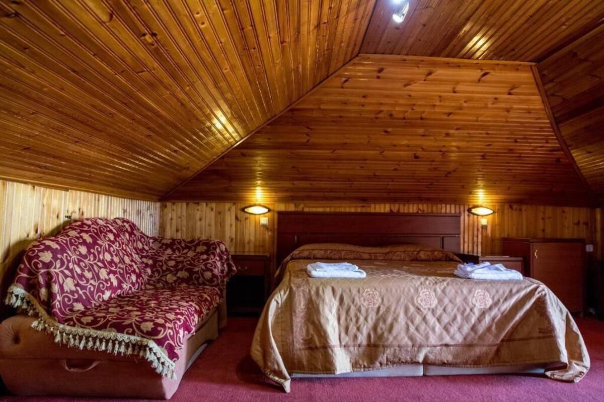 A wooden-paneled room with a bed, a sofa, and two wall-mounted lamps.