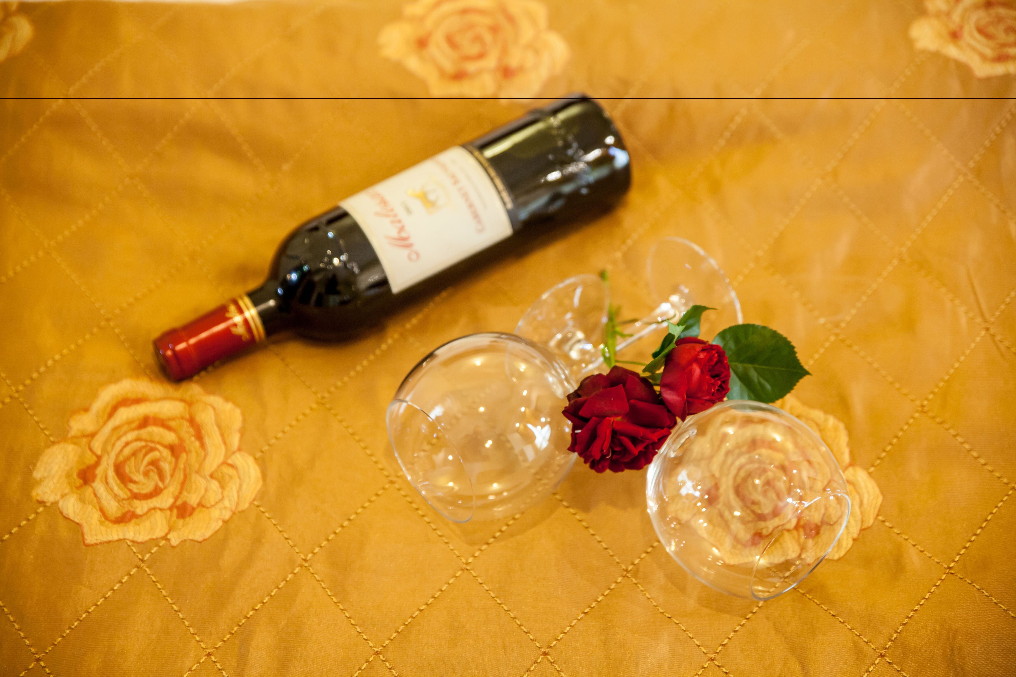 Eine Weinflasche, zwei Weingläser und eine rote Rose auf einer Tischdecke mit Blumenmuster.