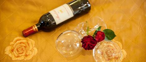 A bottle of wine, two wine glasses, and a red rose on a tablecloth with a floral pattern.