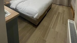 Un dormitorio moderno con cama, mesitas de noche, un espejo y un calefactor empotrado.