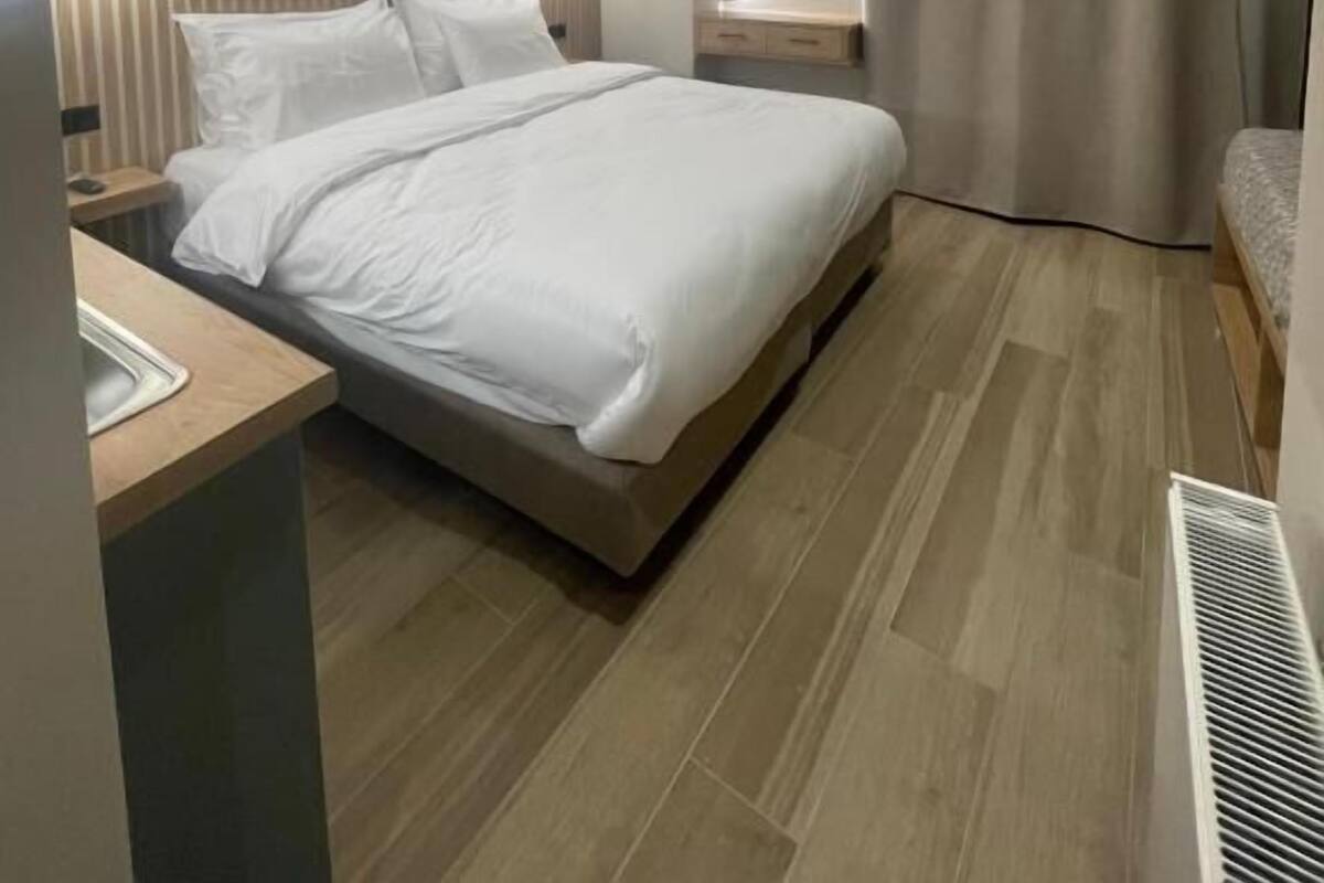 A modern bedroom with a bed, bedside tables, a mirror, and a built-in heater.