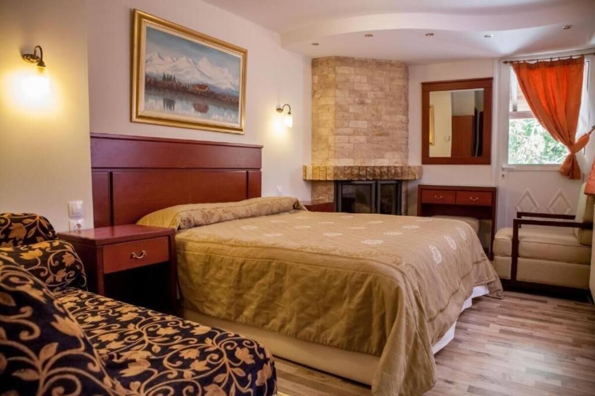 A bedroom with a bed, a nightstand, a dresser, a chair, a fireplace, and a painting on the wall.