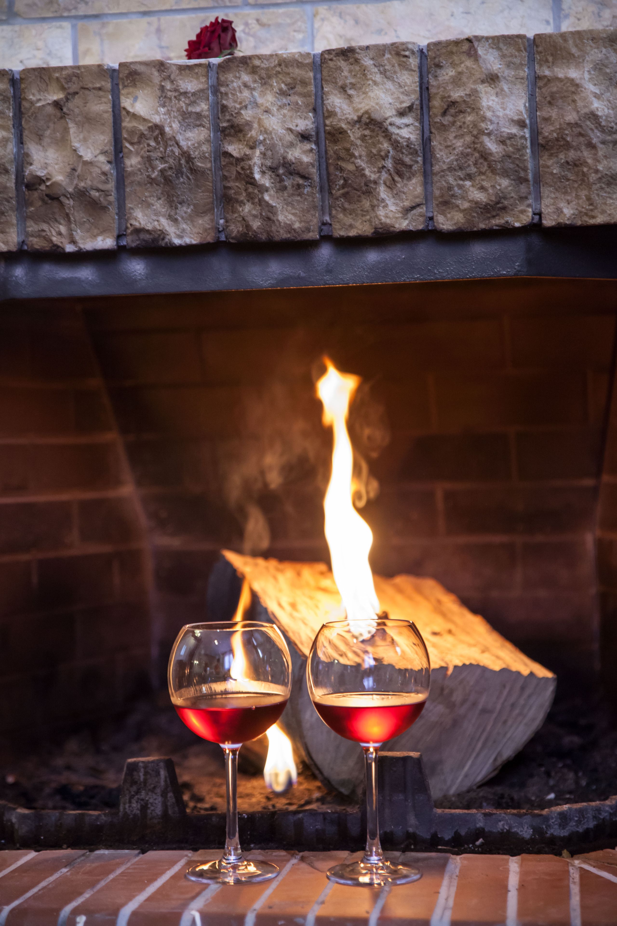 Dos copas de vino tinto frente a una chimenea con leña encendida.