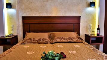 Habitación de hotel con una cama grande, ropa de cama marrón, un ramillete de flores y dos mesitas de noche con lámparas y una botella de vino.