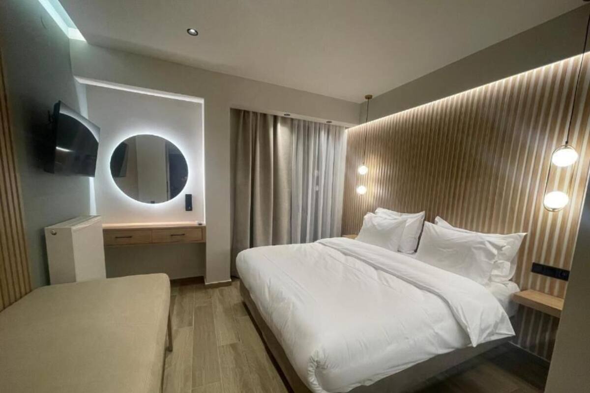 A modern hotel room with a large bed, a desk with a chair, a round mirror, and a TV mounted on the wall.