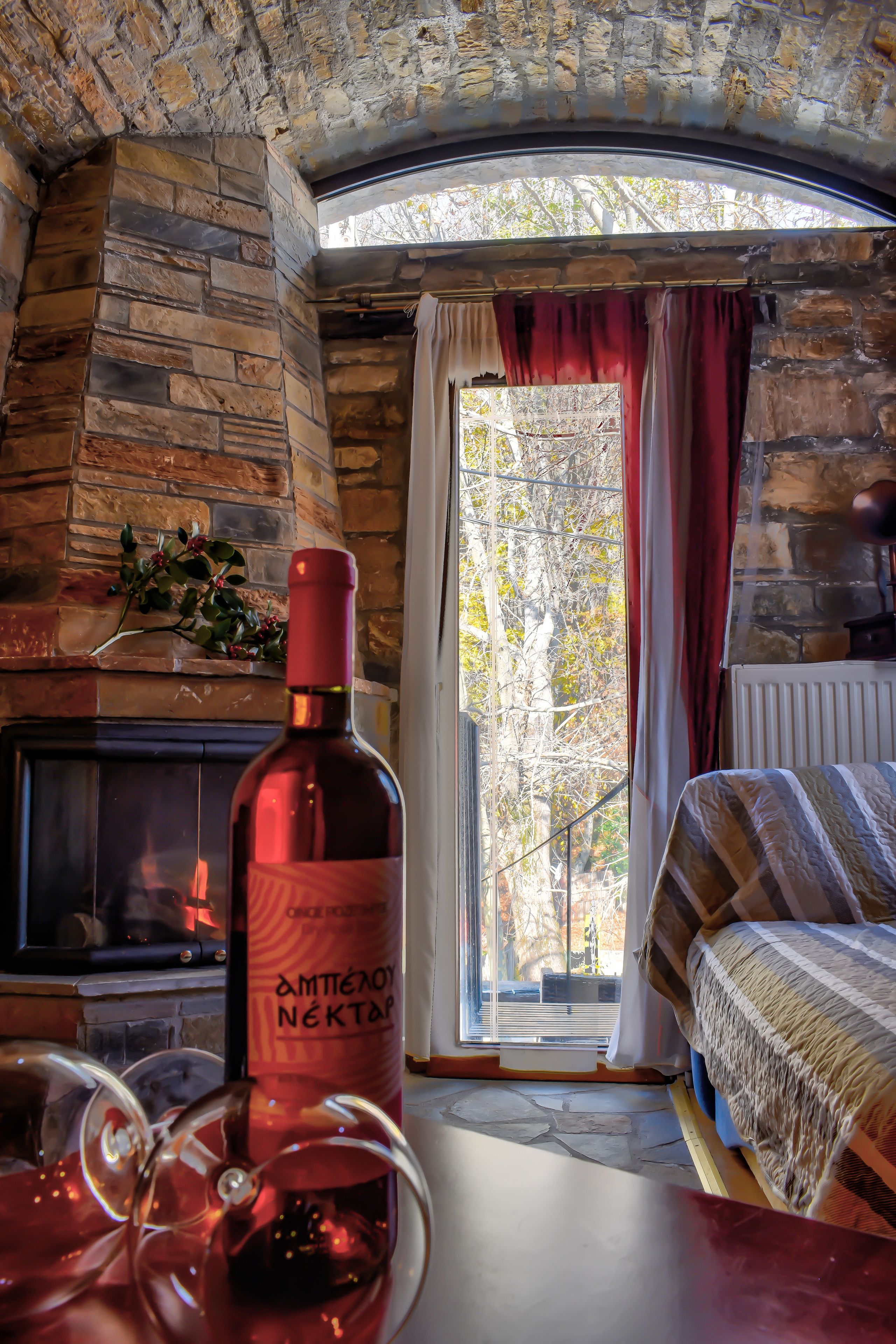 Una habitación con chimenea de piedra, una cama con manta a rayas y una botella de vino sobre una mesa.