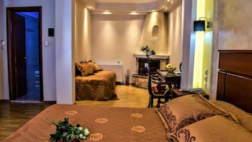 Habitación de hotel con una cama grande, zona de estar con chimenea y vistas al pasillo.