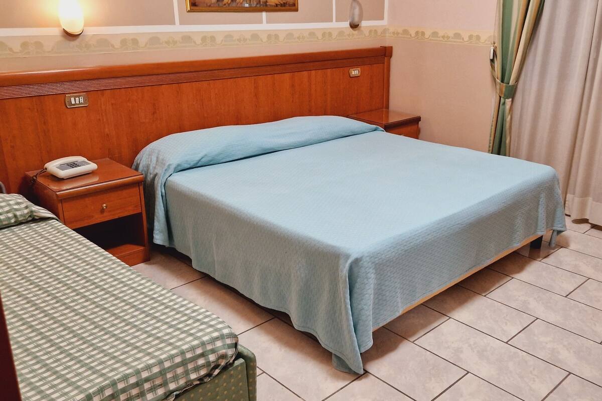 A hotel room with a single bed, a bedside table with a phone, a chair, and a small table with towels.