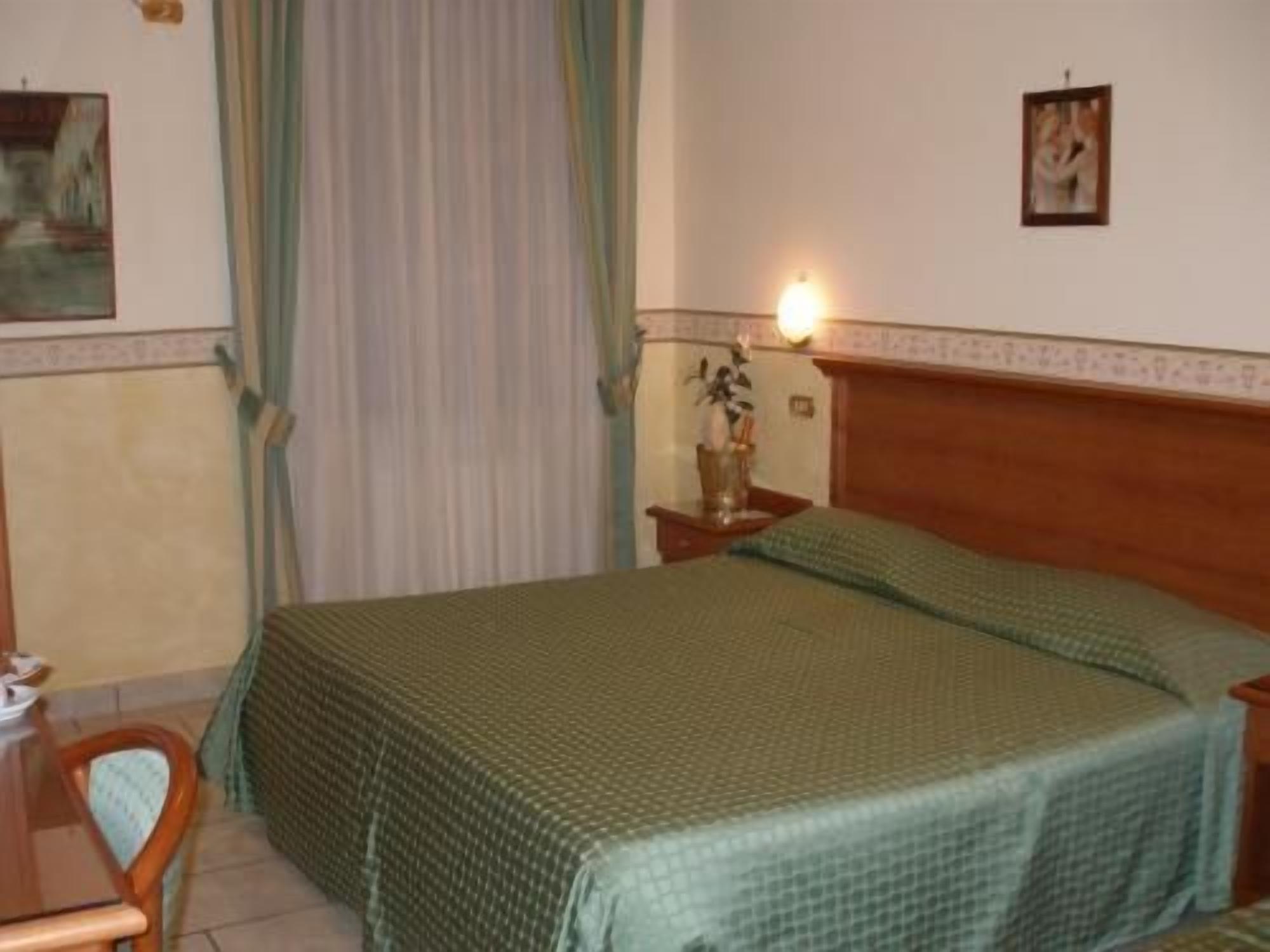Ein Standard-Hotelzimmer mit einem Bett, einem Nachttisch, einem Sessel und einer Wandlampe.