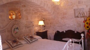 Un dormitorio con pared de piedra, una cama con almohada floral, una lámpara de noche y una lámpara de pared.