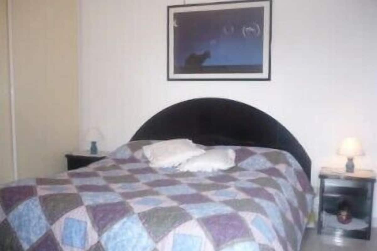 A bedroom with a bed, a nightstand, a lamp, and a framed picture on the wall.