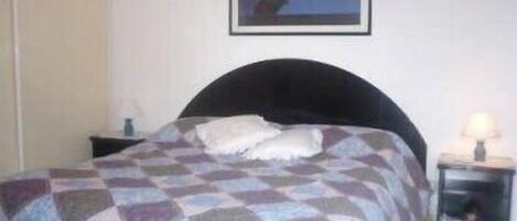 A bedroom with a bed, a nightstand, a lamp, and a framed picture on the wall.