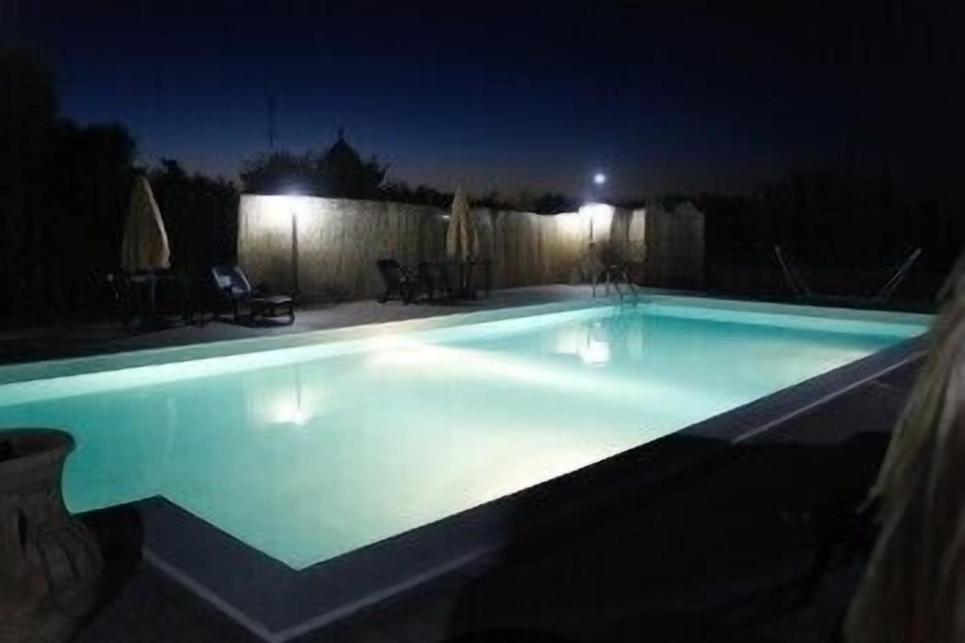 A swimming pool at night with lights around it and lounge chairs.