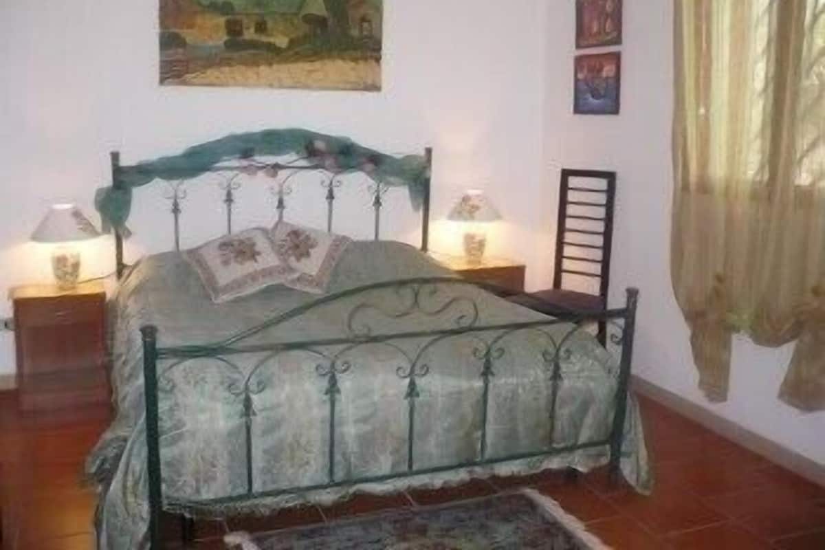 A bedroom with a metal bed frame, two bedside tables with lamps, a chair, and a painting on the wall.