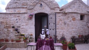 Un edificio de piedra con una cúpula redonda y una puerta de acceso. Hay una mesa con mantel púrpura y sillas afuera.