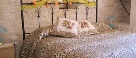 A bed with a leopard print bedspread, a decorative headboard with a yellow and orange design, and two bedside lamps.
