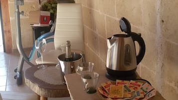 A rustic kitchen with a stone wall, a wooden table with a kettle, a coffee pot, and a basket of tea bags.