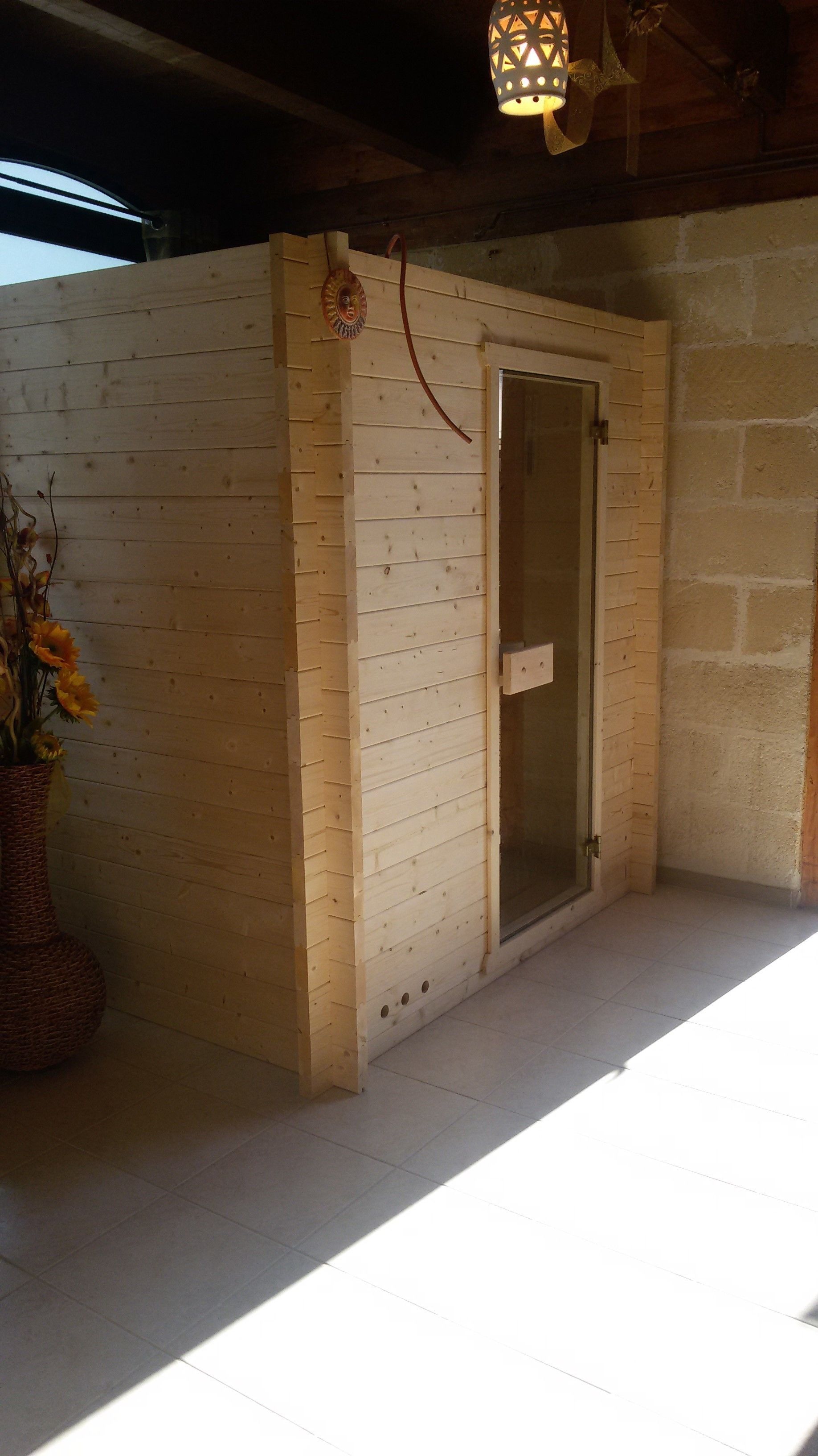 Una habitación de madera con una puerta de cristal, una cesta de mimbre con flores y un farol colgante.