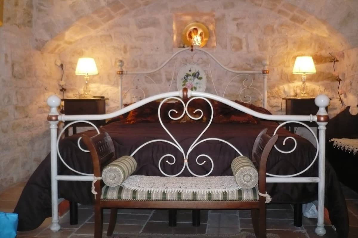 A bedroom with a stone wall, a wooden bed with a decorative headboard, two bedside tables with lamps, and a small decorative item on the wall.