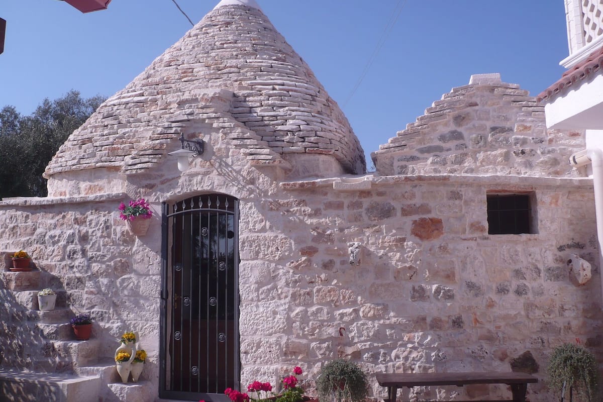 A stone building with a conical roof, a barred door, and potted plants.