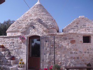 A stone building with a conical roof, a wooden door, and a small window. - L'Isola Felice (Castellana Grotte)