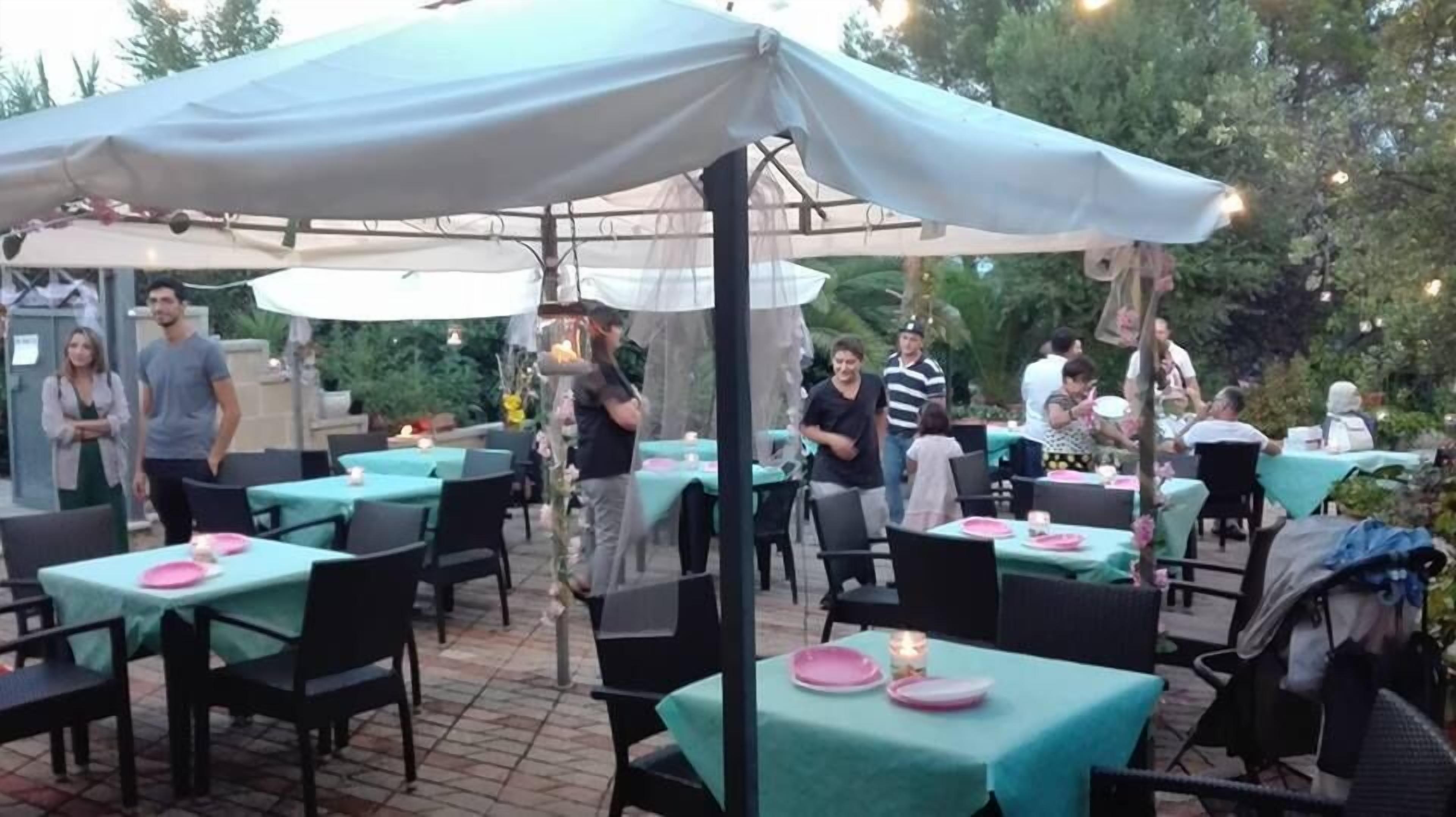 Un área de comedor al aire libre con mesas cubiertas con manteles verdes y sillas negras.