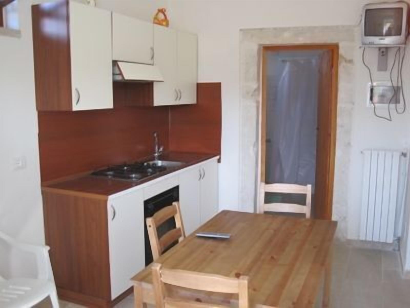Eine kompakte Küche mit weißen Schränken, einer Holz Arbeitsplatte, einem Spülbecken und einem kleinen Fernseher an der Wand.