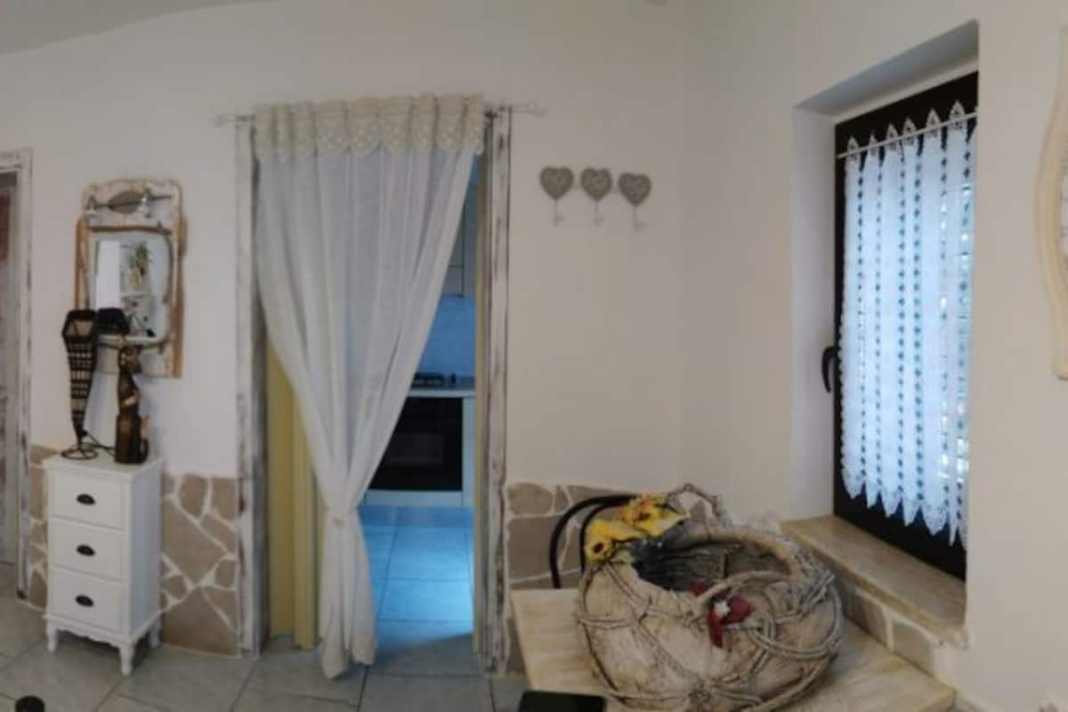 A bedroom with a bed, a dresser, a vanity, a mirror, and a window with curtains.