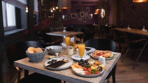 A breakfast setting with a wooden table, plates of food, a basket of bread, and a glass of orange juice. - Hotel am Augustinerplatz (Cologne)