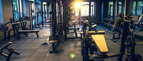 Un gimnasio con diverso equipamiento de ejercicios, amplias ventanas y un suelo de baldosas impecable.