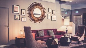 A hotel lobby with a red sofa, two armchairs, a coffee table, a floor lamp, and a wall-mounted mirror. - Hotel am Augustinerplatz (Cologne)