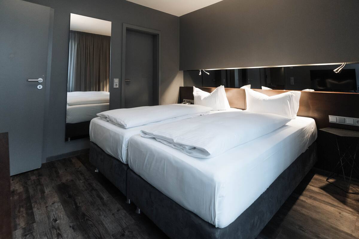 A modern hotel room with a large bed, a bedside table, a mirror, and a door.