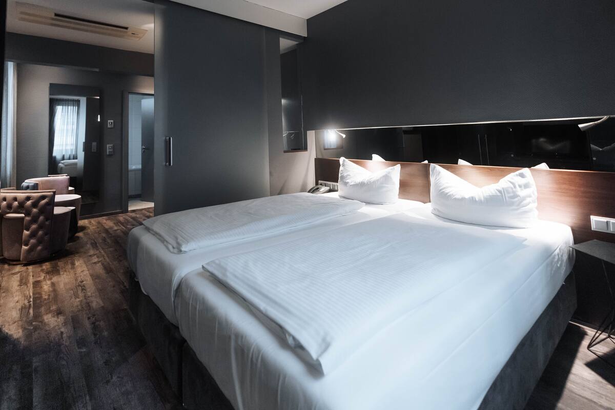 A modern hotel room with a large bed, a bedside table, a chair, and a desk.