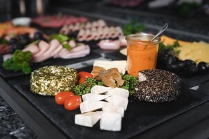 Una tabla de embutidos con diversos quesos, carnes y frutas sobre una base de pizarra.