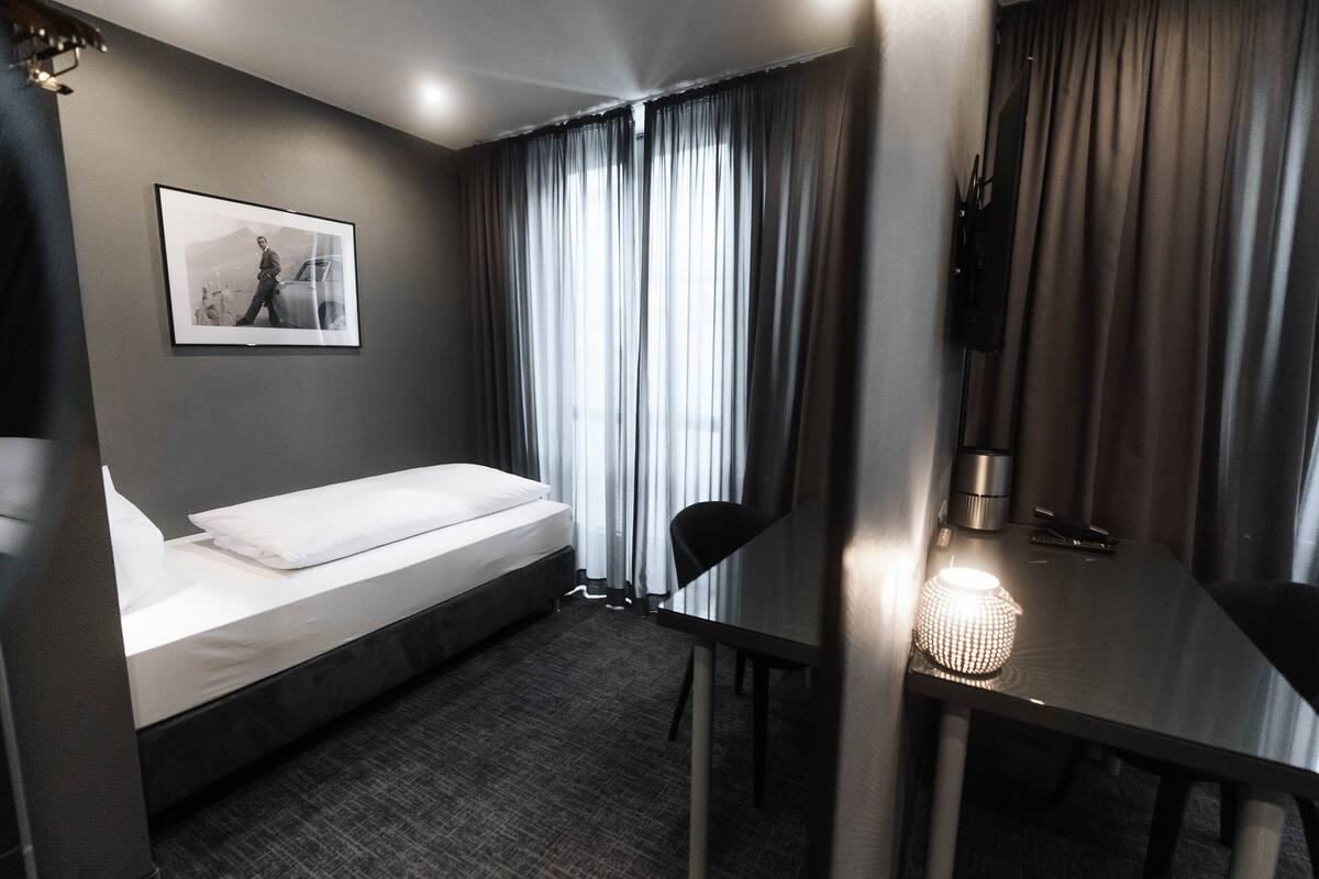 A hotel room with a bed, a desk, a chair, a lamp, and a framed picture on the wall.
