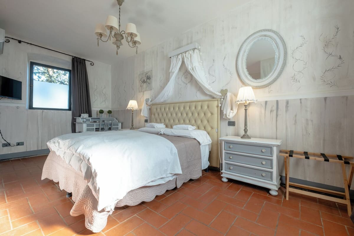 A bedroom with a large bed, a bedside table, a mirror, and a window with curtains.