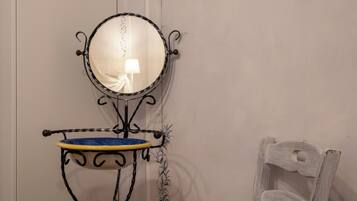 Un baño con un espejo redondo, un lavabo pequeño con un recipiente azul y una silla blanca.