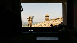A view through a window of a stone wall with two towers, one with a pointed roof and the other with a rounded top.