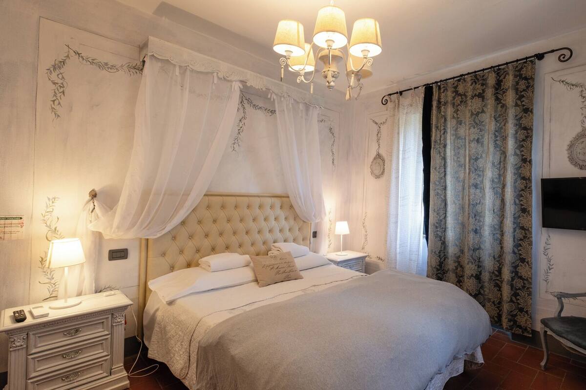 A bedroom with a large bed, a nightstand, a chair, and a television on the wall.