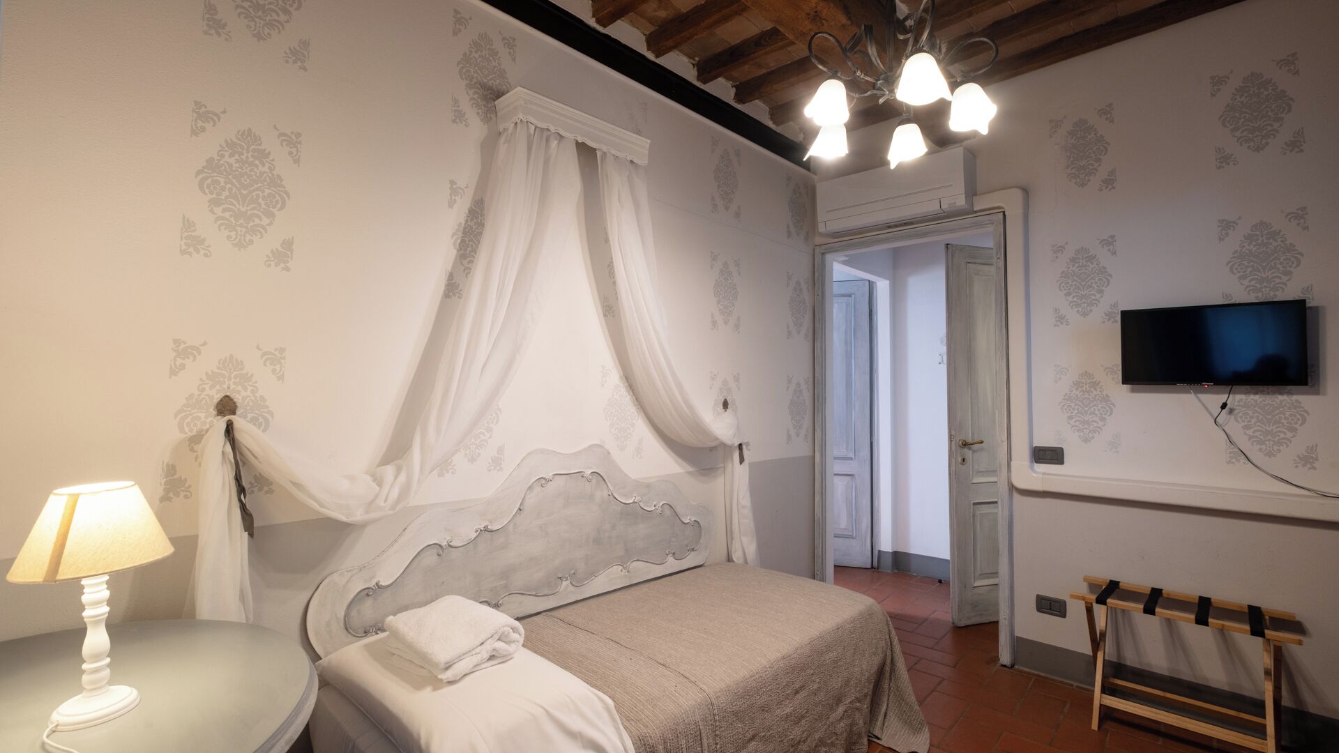 Une chambre à coucher avec un lit, une lampe de chevet, un téléviseur fixé au mur et un banc en bois.