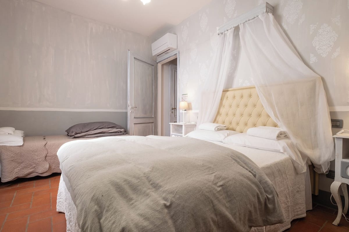 A bedroom with a large bed, a smaller bed, a nightstand with a lamp, and a wardrobe.