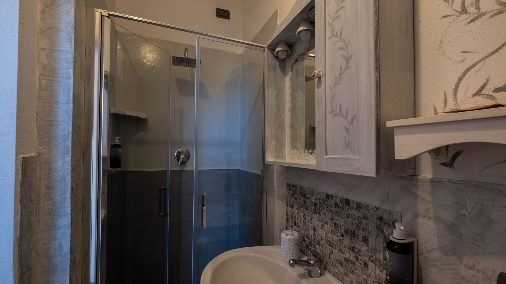 A modern bathroom with a glass shower enclosure, a white sink, and a marble backsplash.