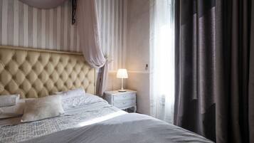 A neatly made bed with a tufted headboard, a bedside table with a lamp, and a window with curtains.